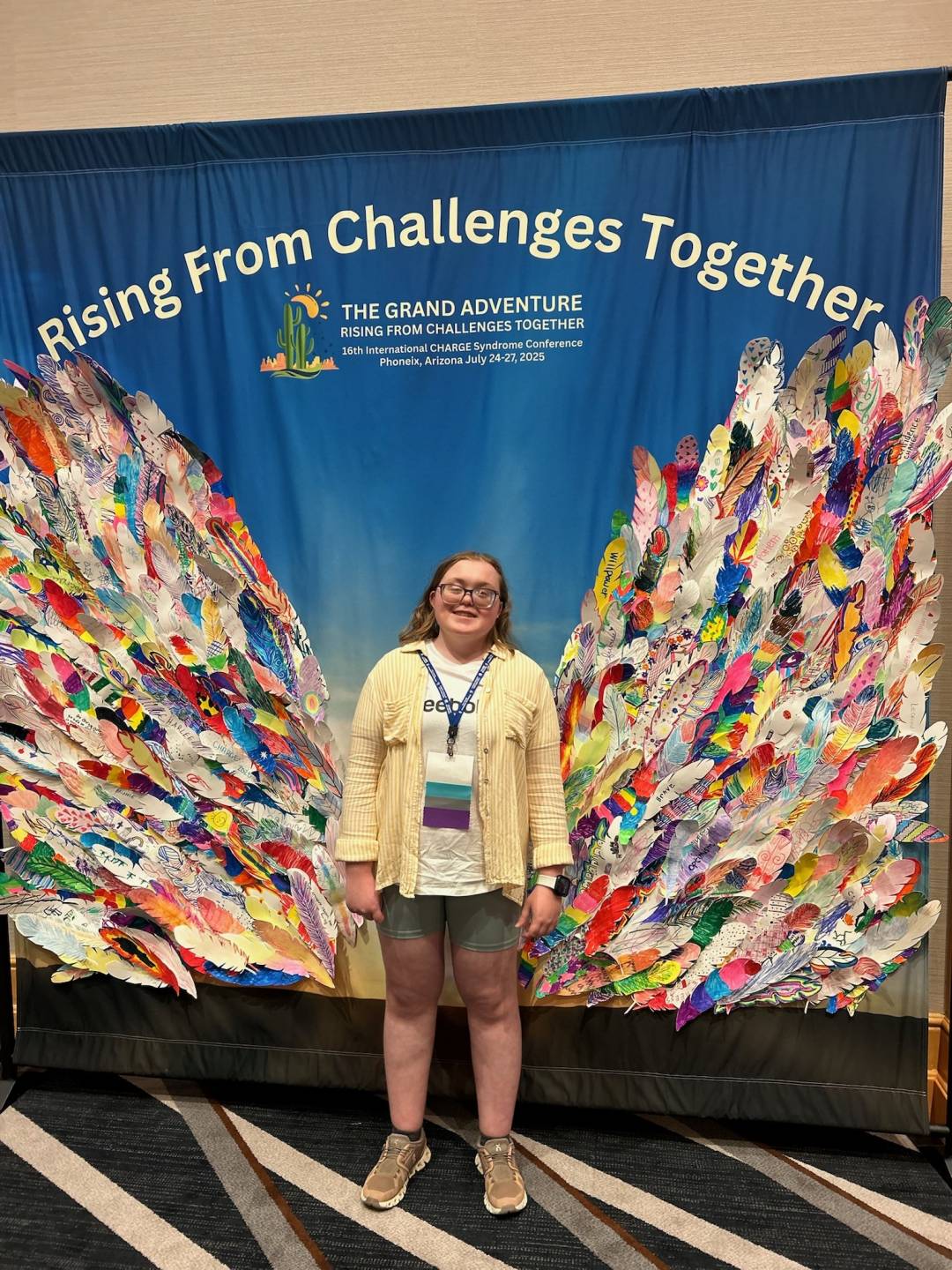 Ryder stands in front of a backdrop that makes it appear she has colorful butterfly wings. Words on the banner behind her read "rising from challenges together."